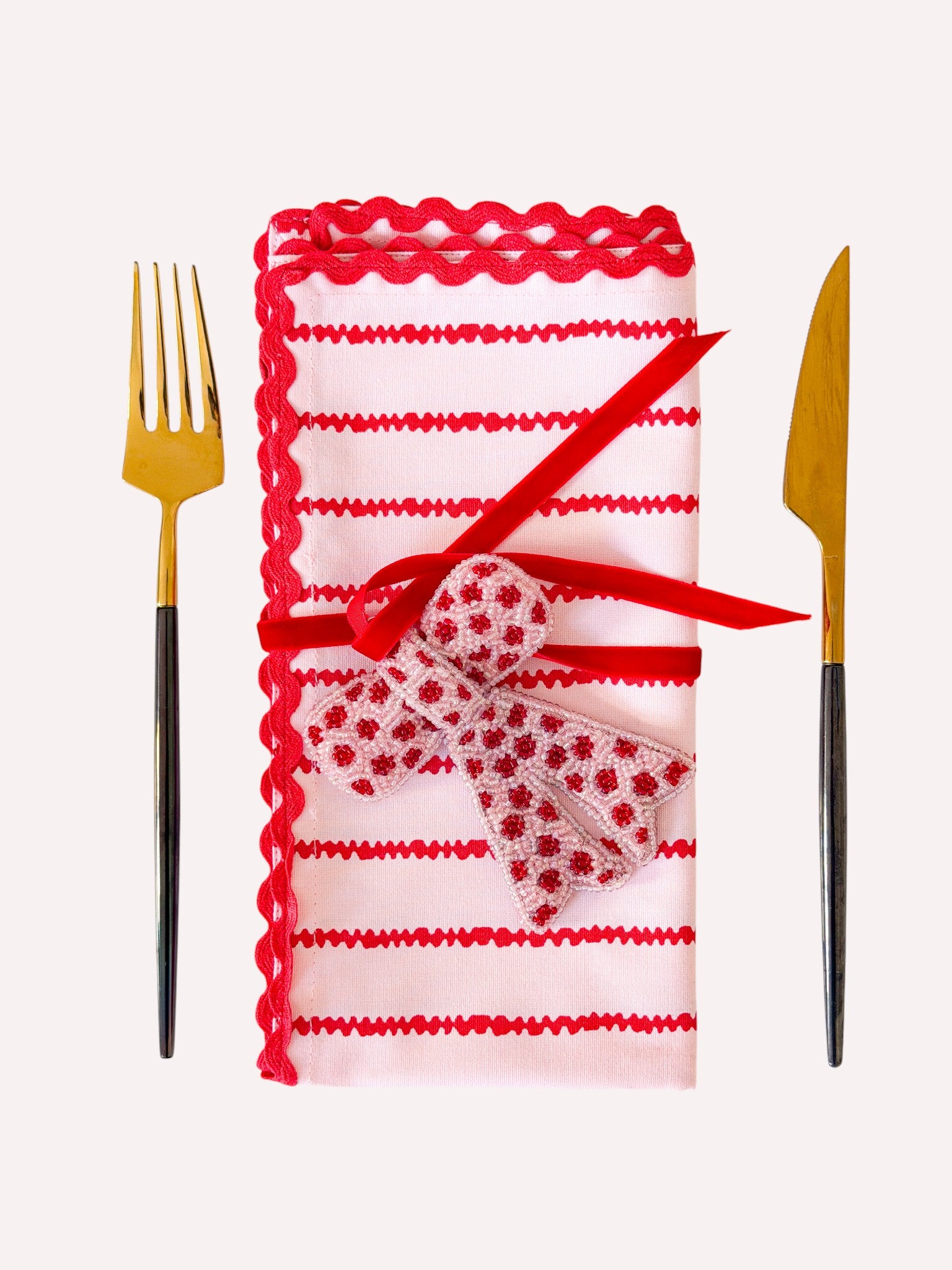 Candy cane colored Christmas napkin decorated with a bow ornament and a velvet ribbon
