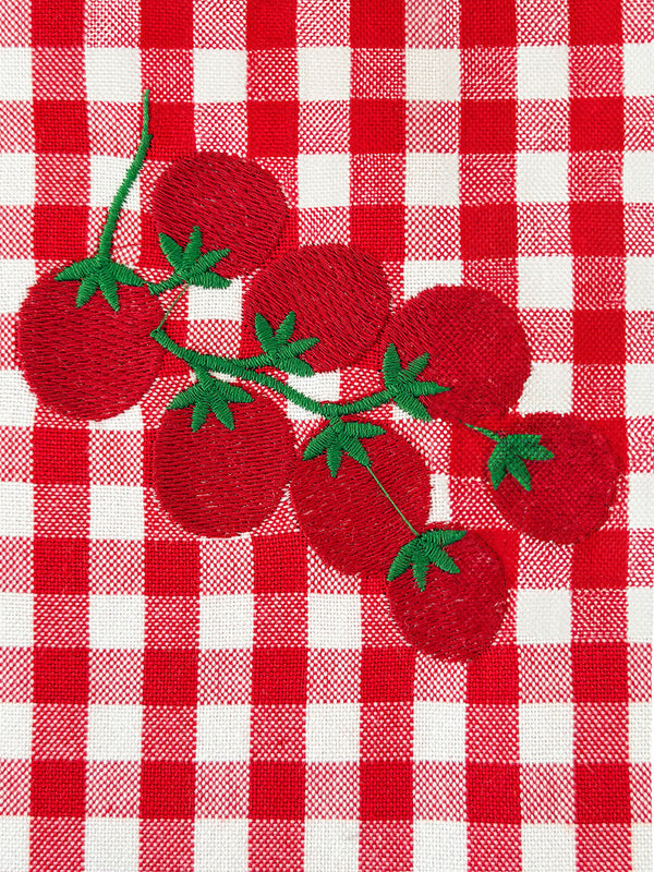 Close-up of intricate hand-guided embroidery on a premium red and white checkered organic cotton fabric.